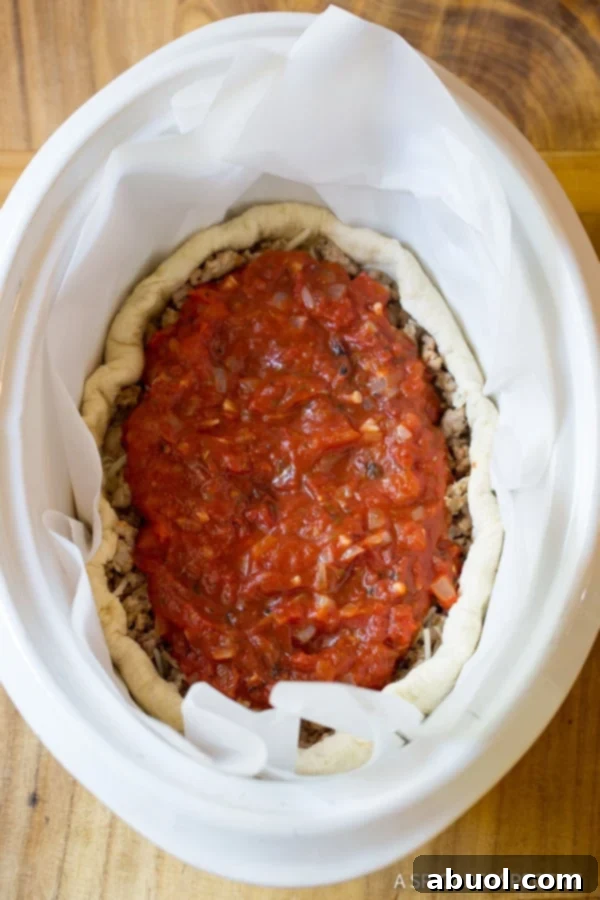 A top down view of the slow cooker deep dish pizza, with the vibrant tomato sauce spread over the sausage and cheese layers, ready for cooking.