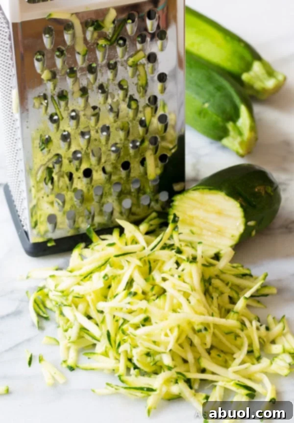 Freshly grated zucchini, the primary ingredient, collected in a bowl and ready for moisture removal, highlighting the preparation step for healthy baked zucchini tots.