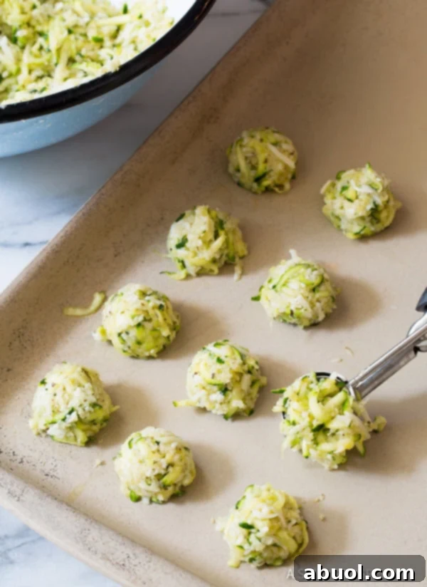 Small, neatly shaped zucchini tots arranged on a parchment-lined baking sheet, prepared for baking until golden and crispy.