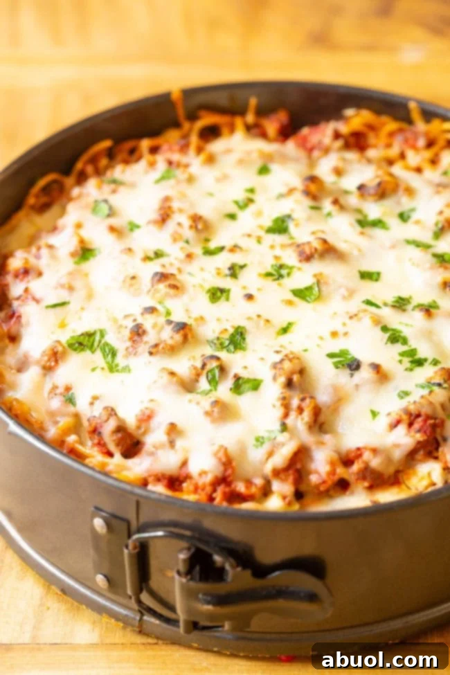 A whole baked spaghetti pie, fresh from the oven, with a golden-brown cheesy top and crispy edges, sitting on a wooden cutting board.