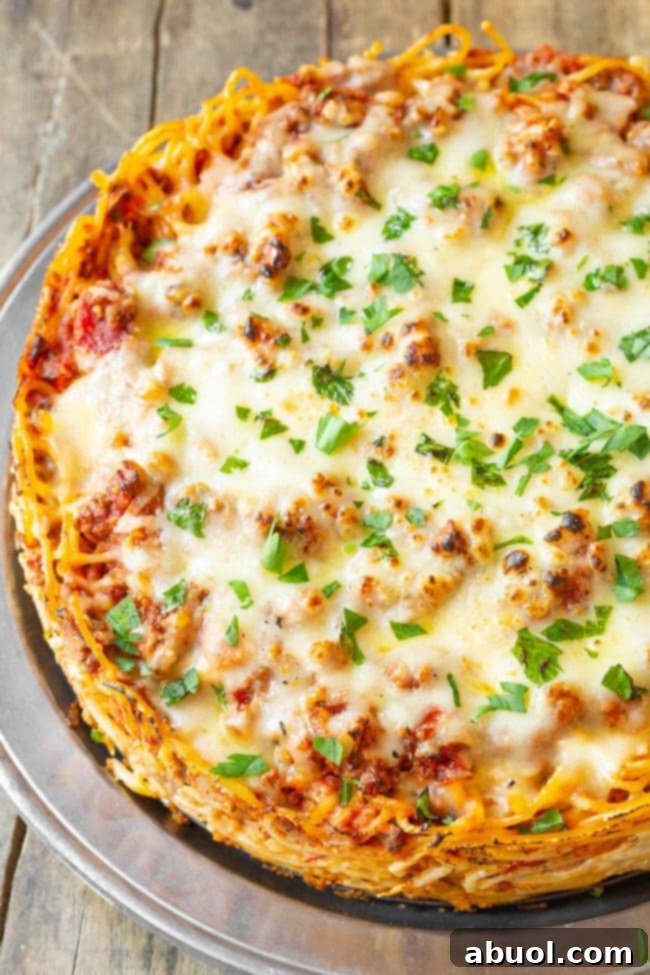 A close-up of the baked spaghetti pie, showing the vibrant red meat sauce and melted cheese topping with steam rising.
