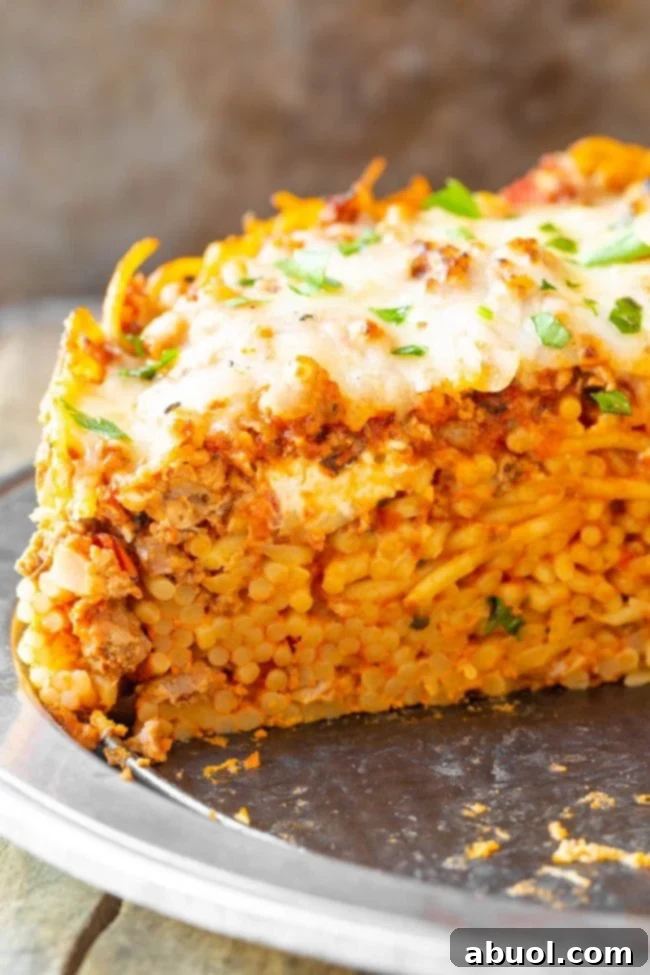 A freshly cut slice of baked spaghetti pie, revealing the distinct layers of pasta, creamy filling, and meat sauce, served on a plate.