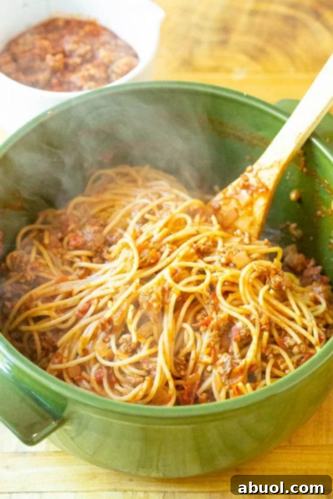Al dente spaghetti noodles being drained in a colander after cooking, ready to be mixed with the meat sauce for the spaghetti pie.