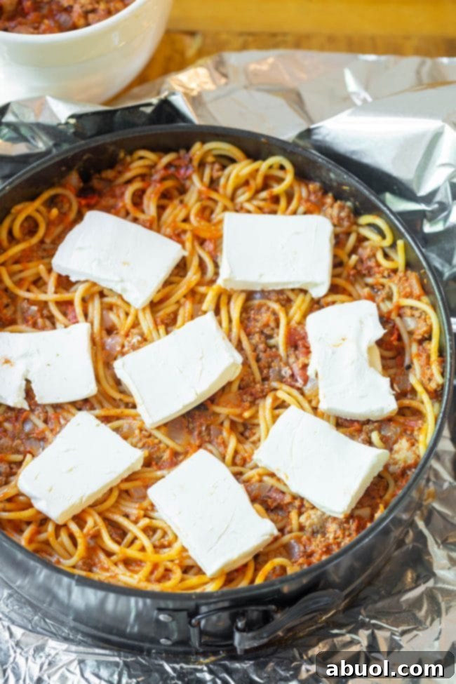 Cooked spaghetti noodles being mixed thoroughly with the savory meat sauce in a large pot, ensuring every strand is coated.