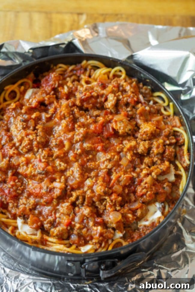 Beaten eggs being stirred into the spaghetti and meat sauce mixture, acting as a binder for the pie base.