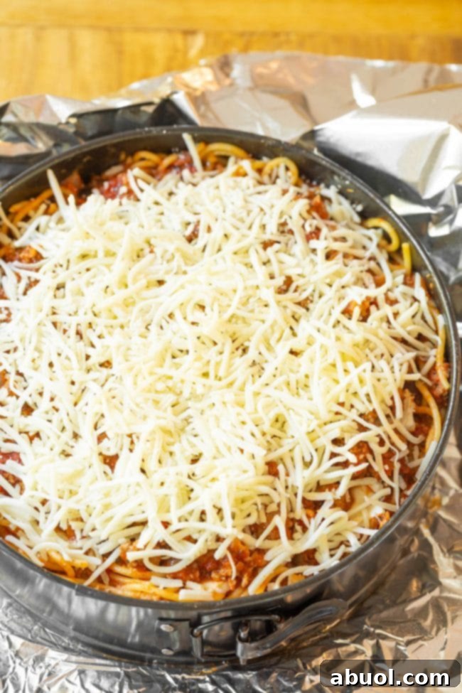 Thin slices of cream cheese being carefully arranged over the packed spaghetti base in a springform pan, creating the hidden creamy layer.
