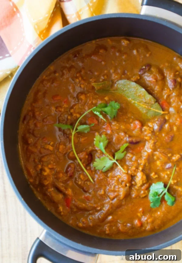 Overhead view of a steaming pot of pumpkin chili, ready to be served, garnished with fresh herbs.
