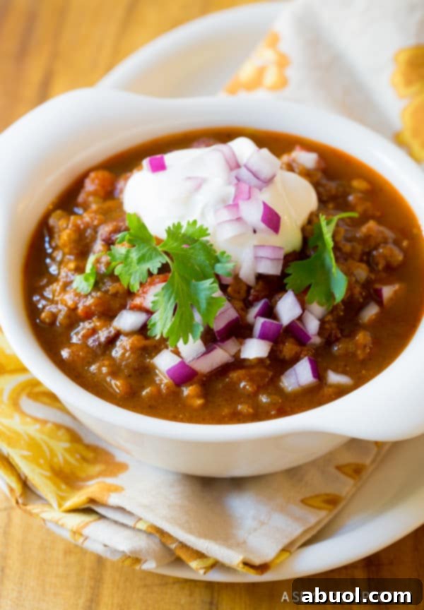 A pristine white bowl filled with pumpkin chili, beautifully arranged with a medley of toppings including fresh cilantro, sour cream, and diced red onion.