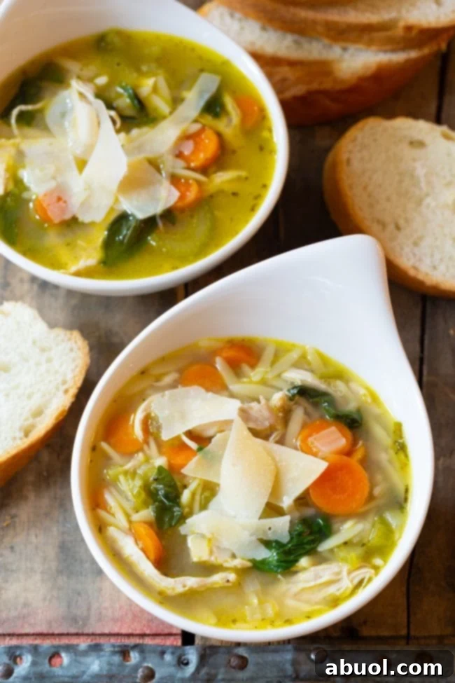 Overhead shot of two bowls of Italian Chicken Orzo Soup, garnished with fresh basil, with slices of crusty bread arranged around them on a wooden table.