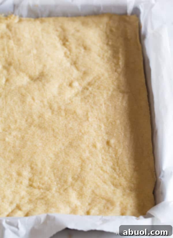 Shortbread cookie crust expertly pressed into a baking pan lined with parchment paper, ready for baking.