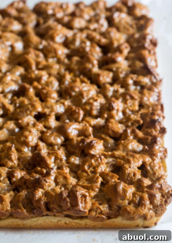 Freshly baked pecan pie bars, uncut on parchment paper, displaying a perfectly golden top.