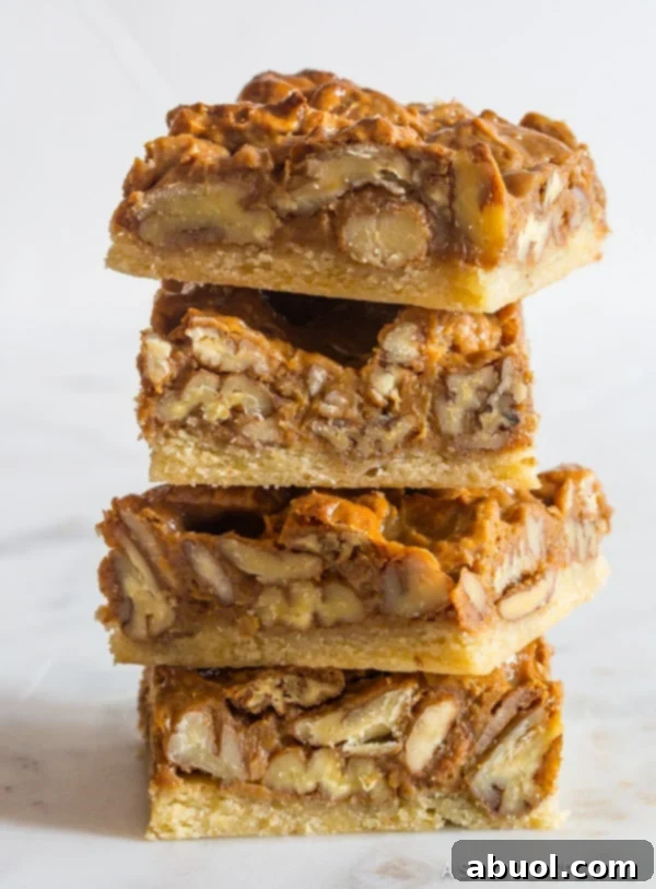 Pecan pie bars stacked to reveal their distinct, delicious layers: a buttery crust and a gooey pecan topping.