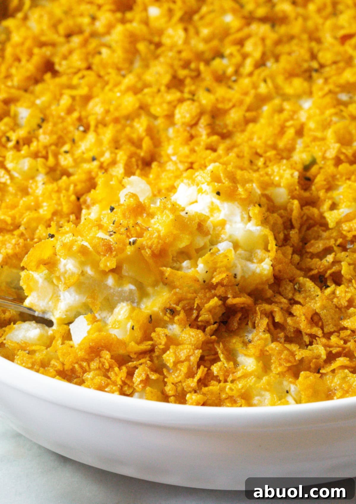 A generous scoop of Company Potatoes casserole on a plate, with the baking dish and serving spoon blurred in the background, ready to be enjoyed.