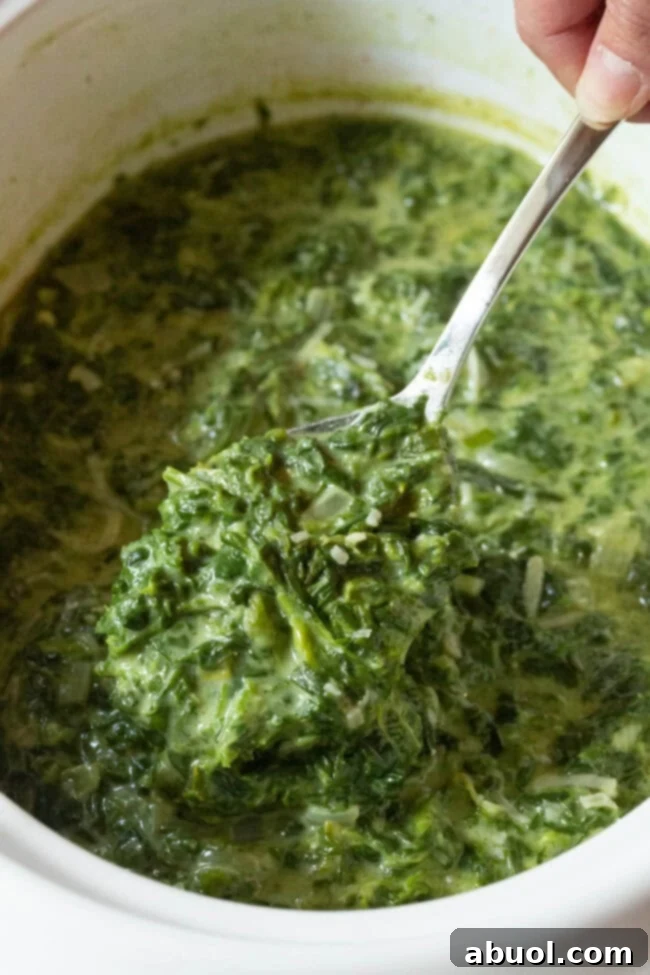 Creamed spinach in a crock pot with a large spoon taking a scoop.