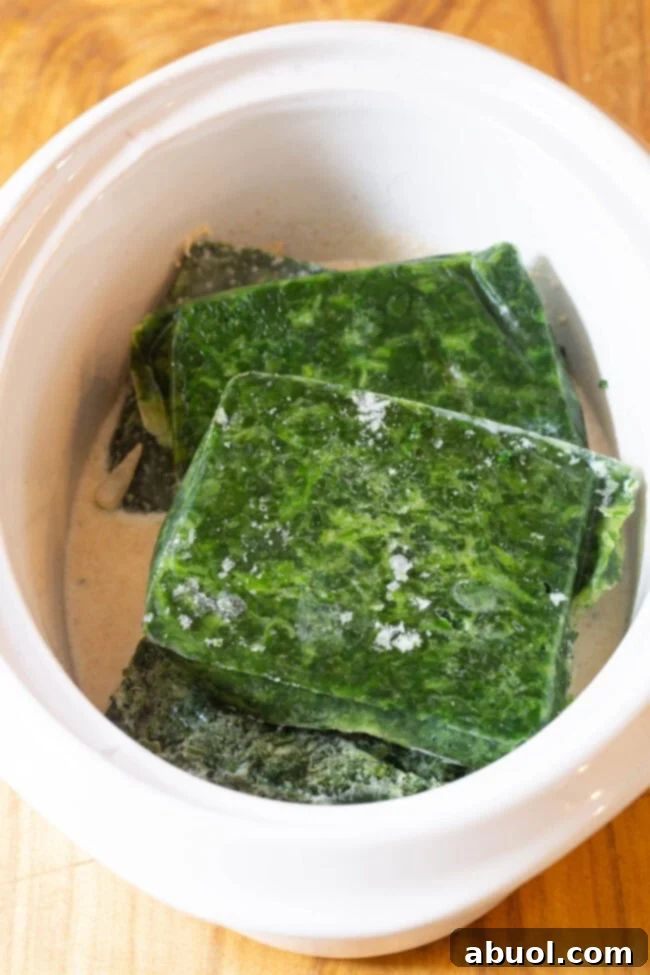 Frozen Spinach is placed in the slow cooker on top of the onions and cream mixture.