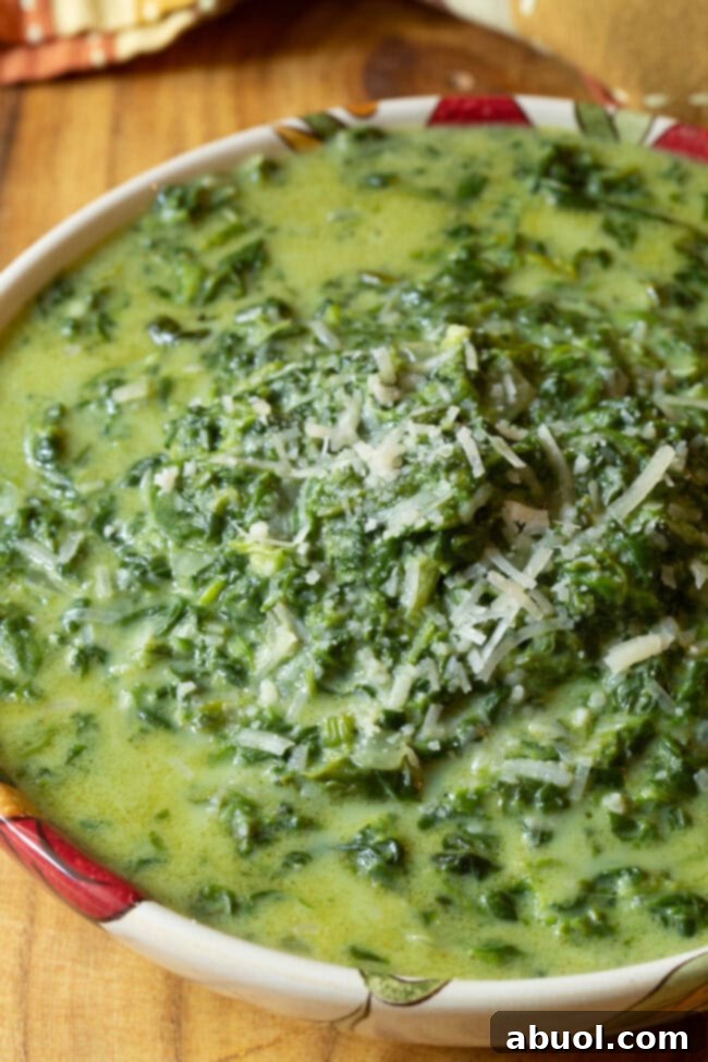 Slow Cooker Creamed Spinach with some cheese sprinkled on top in a serving bowl.
