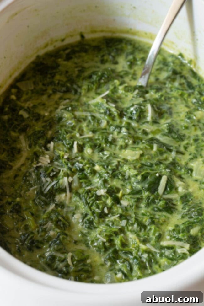 Top view of the inside of crockpot with creamed spinach in it with a spoon ready to serve.