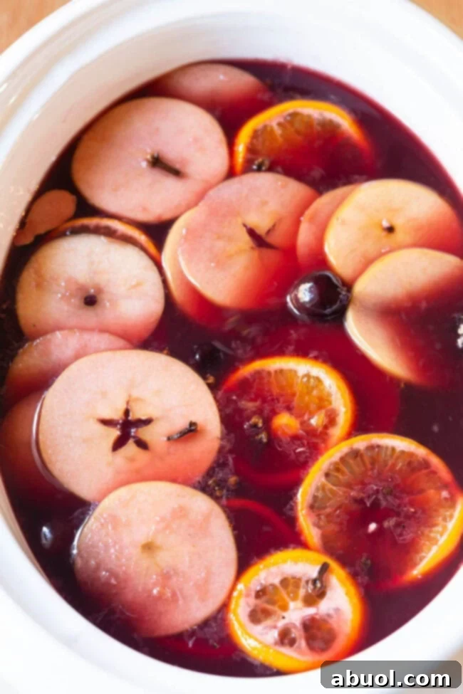 Crockpot Mulled Wine (Wassail) with sliced oranges, apples, and cinnamon sticks floating in a slow cooker.