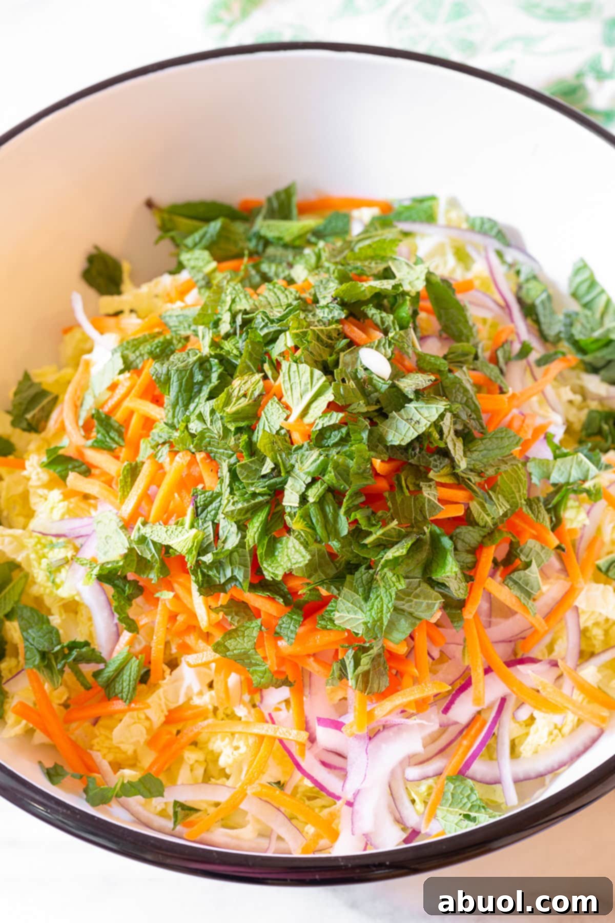 Freshly chopped vegetables including lettuce, cabbage, onion, carrots, and an assortment of fresh herbs in a large mixing bowl, ready for the salad base.