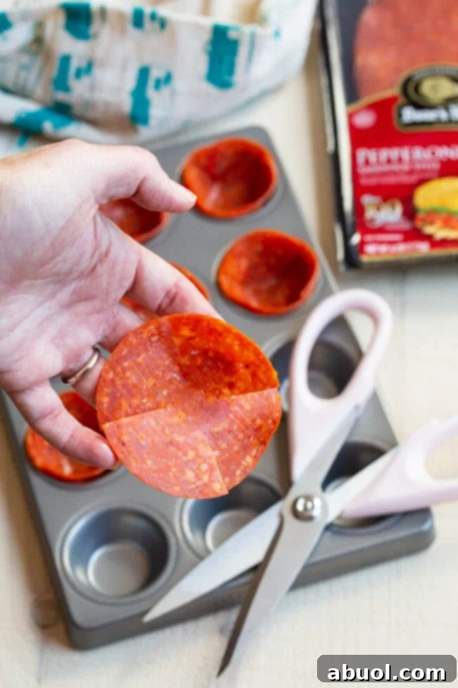 Preparing Pepperoni for Pizza Cups A hand holding a large pepperoni slice with four small cuts made around its edges, preparing it for shaping.