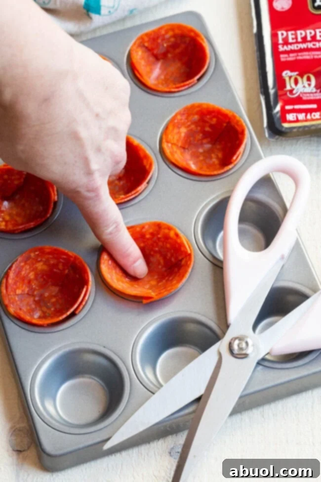 Keto Pepperoni Pizza Bites 3 A finger gently pressing a cut pepperoni slice into a mini muffin tin well to form a cup shape.
