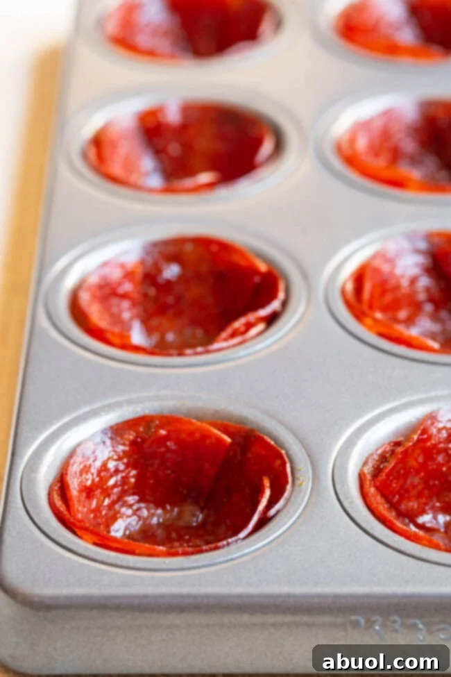 Keto Pepperoni Pizza Bites 4 Pepperoni cups baking in a mini muffin tin, edges crisping up beautifully.
