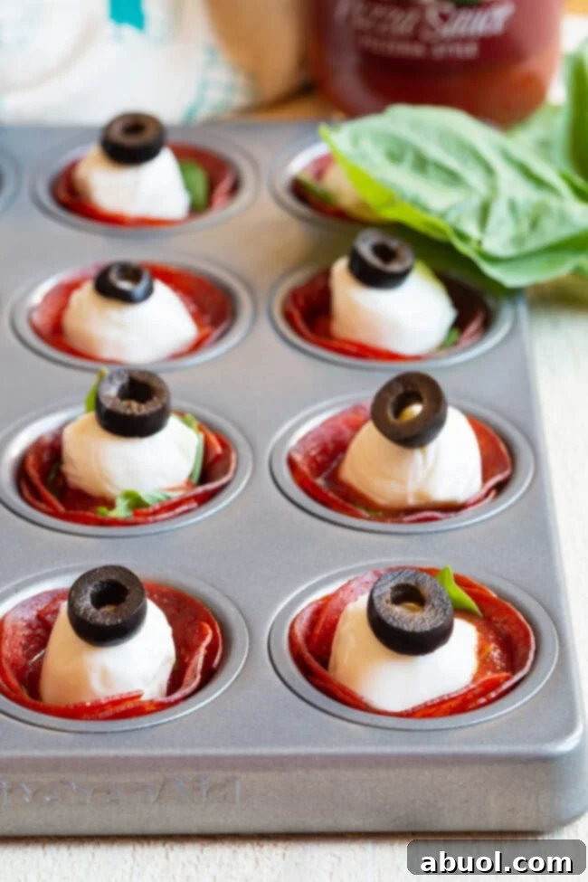 Assembled Pepperoni Pizza Cups Pepperoni cups filled with pizza sauce, a mini mozzarella ball, and a black olive slice.