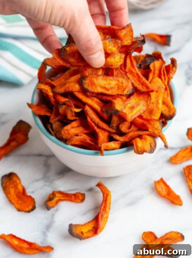 Snacking on healthy carrot chips A hand reaching for a crispy baked carrot chip from a bowl.