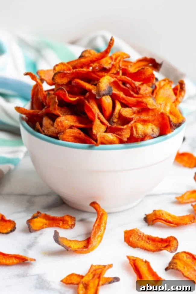 Crispy Baked Carrot Crisps 3 Baked carrot chips served in a rustic bowl, with some scattered on a wooden surface.