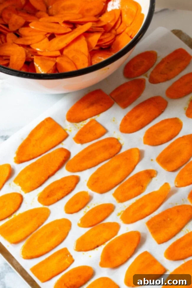 Crispy Baked Carrot Crisps 7 Seasoned carrot slices spread in a single layer on a parchment-lined baking sheet.