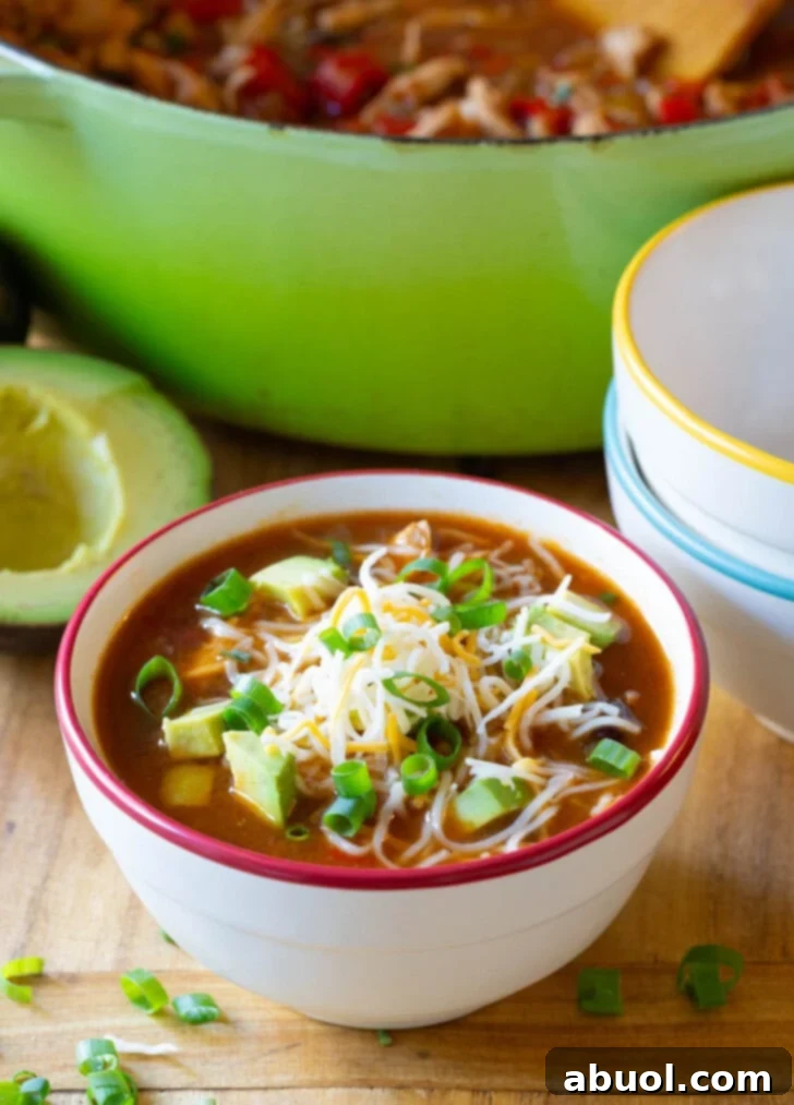 Fajita soup in a bowl with shredded cheese, sliced scallions and diced avocado.