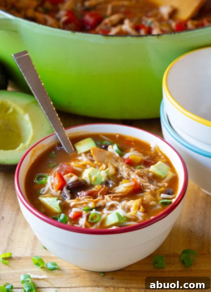 Soup in a bowl with shredded cheese, sliced scallions and diced avocado.