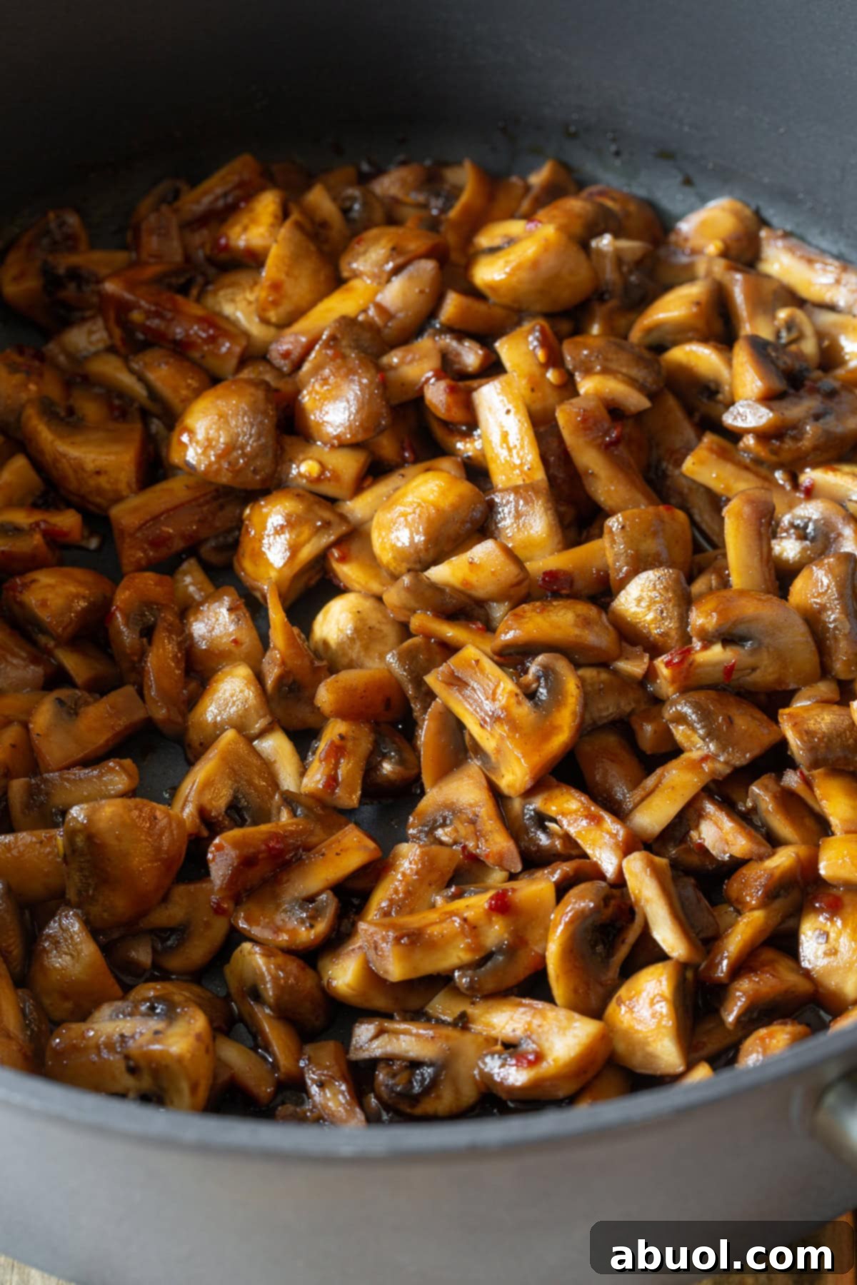 Close-up shot of Asian stir-fried mushrooms sizzling in a large, hot skillet, their surfaces caramelized and coated in a rich, dark sauce, with steam gently rising.