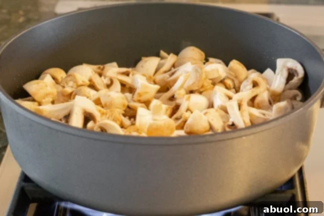 Finely diced button mushrooms being expertly cooked in a large, hot skillet, showing early stages of browning and caramelization as they release moisture.
