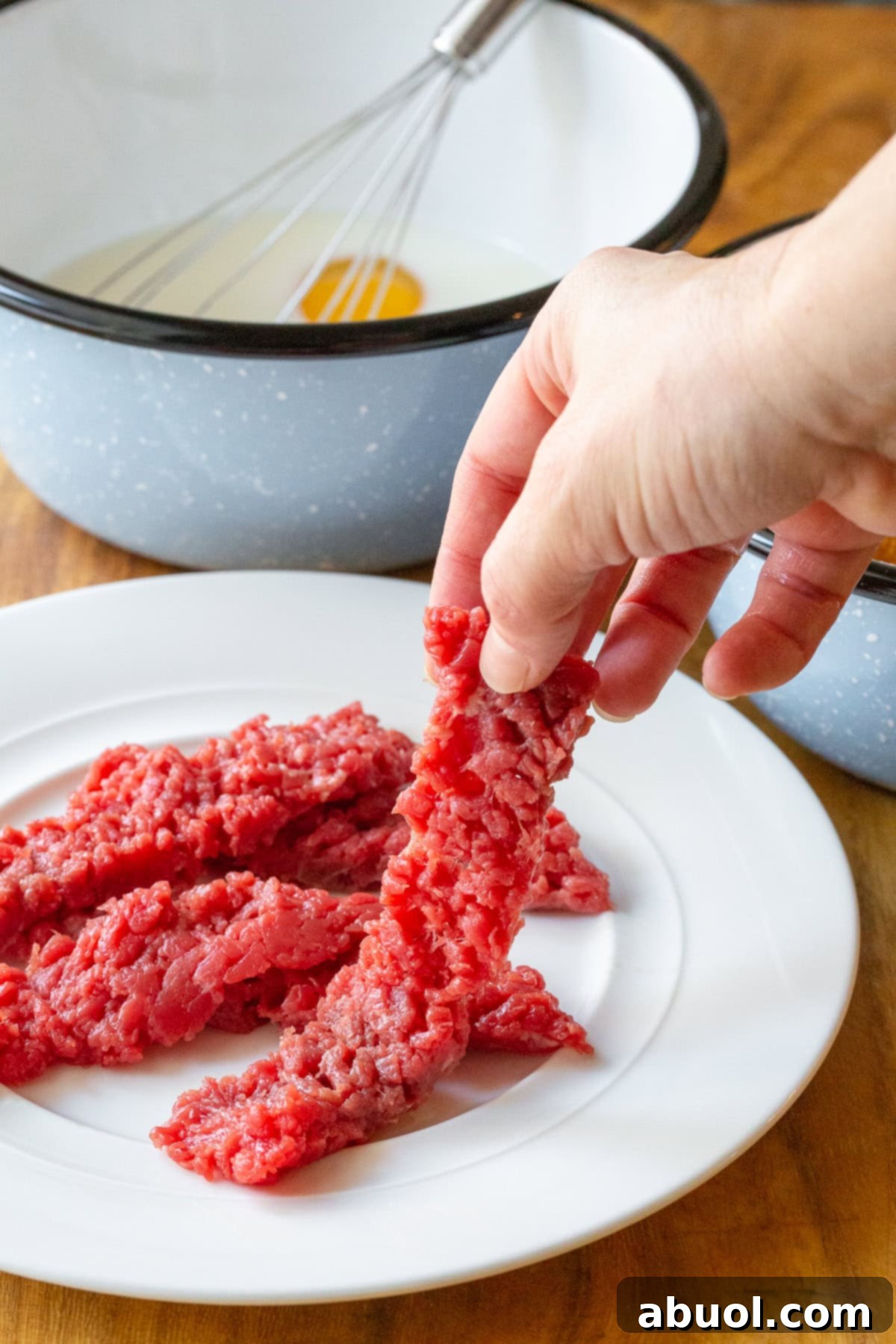 A hand gently holding a piece of raw, tenderized cube steak, ready to be prepared for breading and frying into crispy steak fingers.