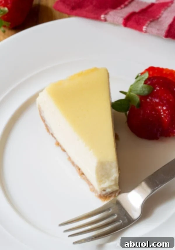 Dreamy Slow Cooker Cheesecake 8 A top-down shot captures a slice of slow cooker cheesecake with a bite removed, accompanied by a fork and a fresh strawberry, tempting the viewer.