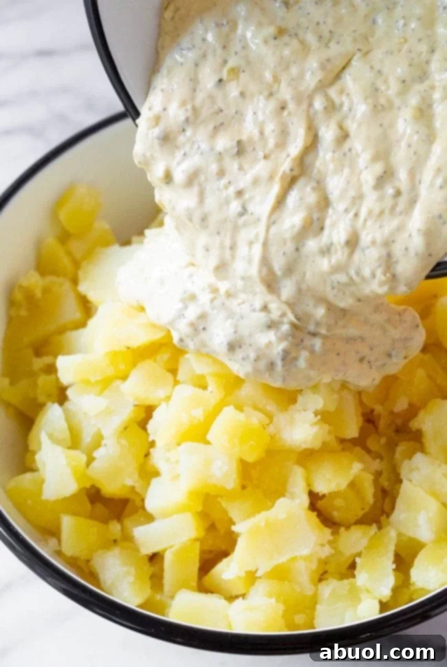 Creamy dressing poured over fluffy, chopped potatoes, ready to be mixed for the best potato salad.