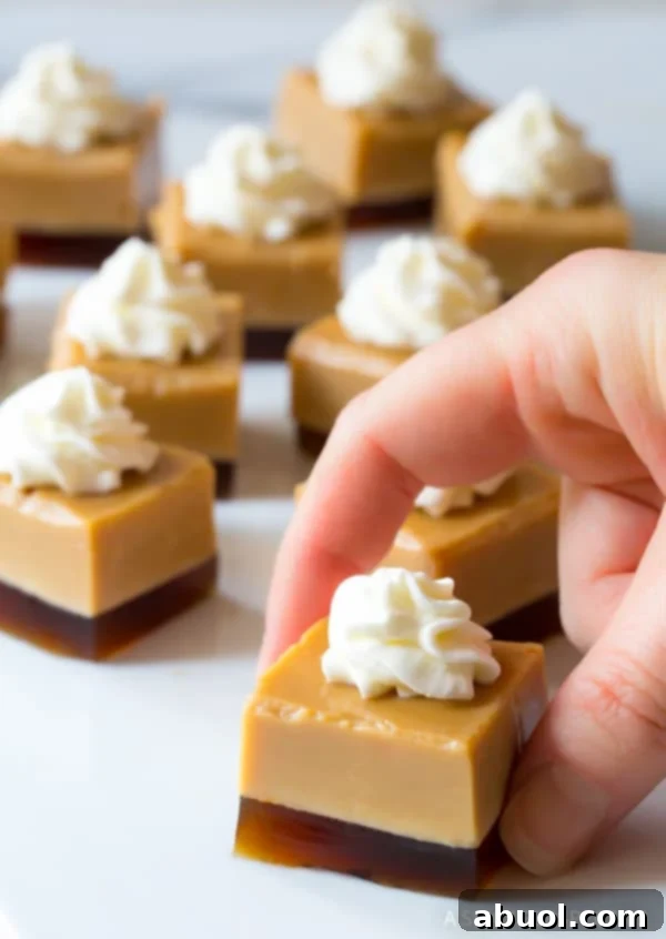 A hand holds a perfectly cut square Baileys Irish Cream Jello Shot, topped with a swirl of whipped cream, showcasing its distinct layers.