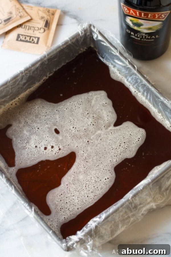 A square baking dish lined with plastic wrap, holding a dark layer of coffee gelatin, chilling in the refrigerator.
