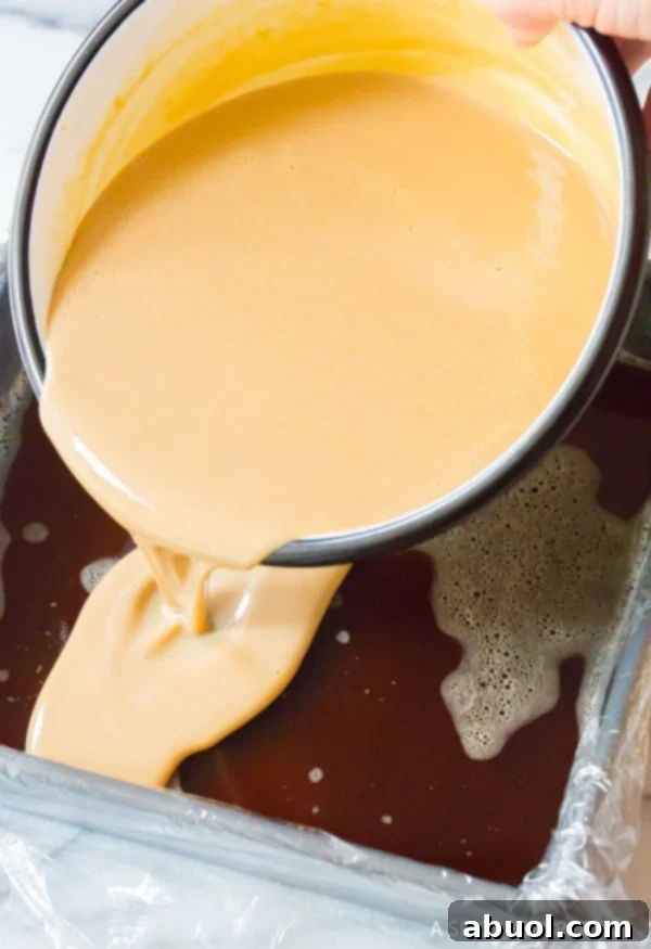 The creamy Baileys Irish Cream mixture being carefully poured over the set coffee gelatin layer in a baking dish.