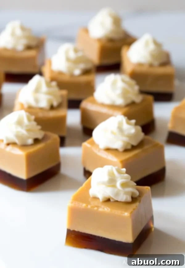 A collection of perfectly cut Baileys Irish Cream jello shot squares, each with a distinct coffee layer and a generous dollop of whipped cream, arranged on a serving platter.