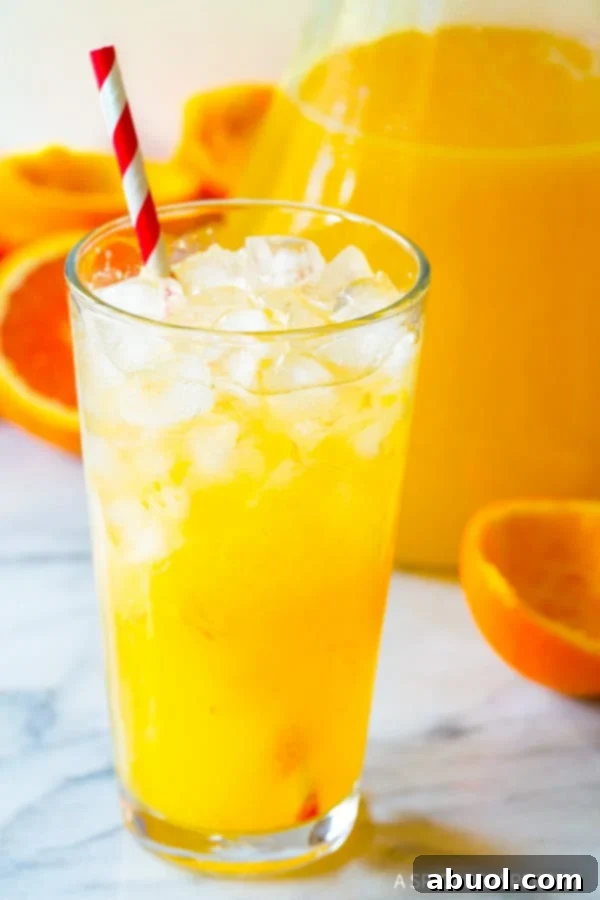 A close-up of a pint glass filled with vibrant orangeade and ice, adorned with a festive red and white striped straw, ready to be enjoyed.
