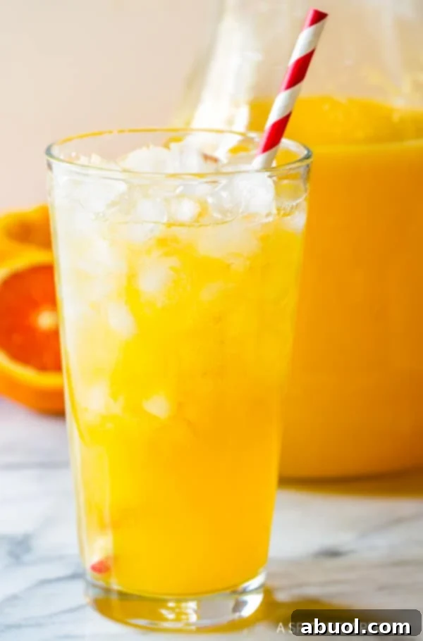 A glass filled with ice and the homemade Southern orangeade, garnished with a citrus slice and a red and white striped straw, beckoning for a refreshing drink.