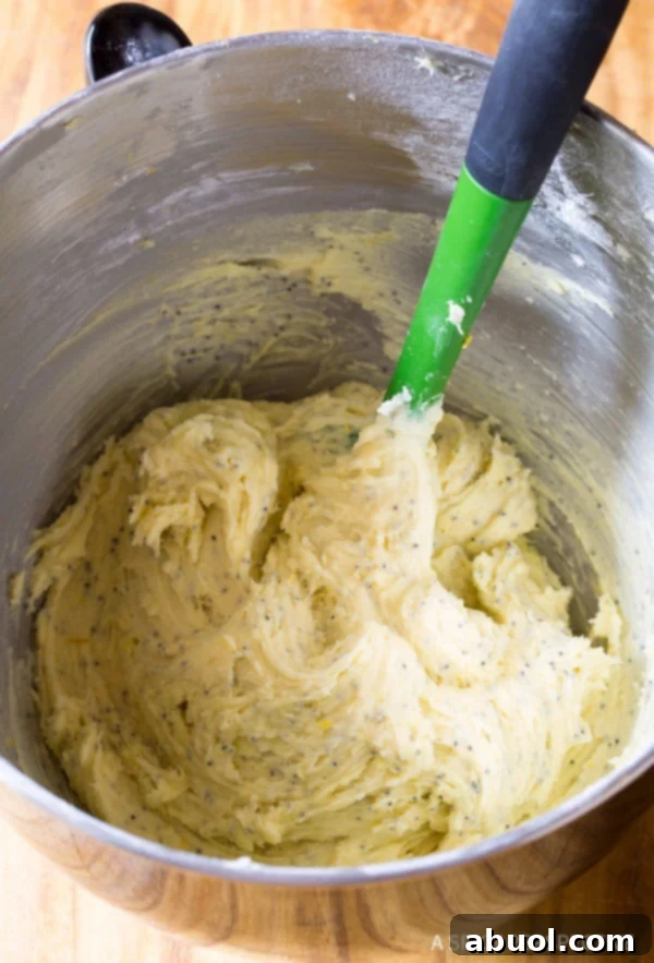 Lemon cookie dough being mixed in a stand mixer bowl with a rubber spatula, showing its creamy texture.