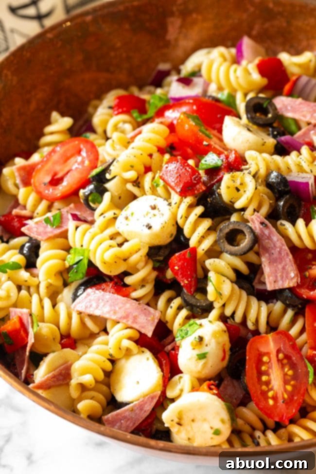 An overhead shot of the finished Italian pasta salad in a large elegant serving bowl, showcasing its rich colors and abundance of ingredients. It's ready for serving at a gathering.