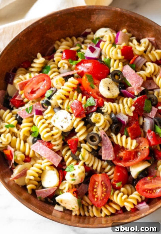 A close-up view of the prepared Italian pasta salad, showcasing the spirals of fusilli pasta, halved cherry tomatoes, salami slices, mini mozzarella balls, and chopped olives, all generously coated in dressing.