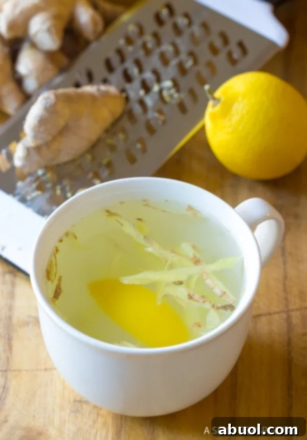 Lemon ginger tea in a cup. A clear glass mug filled with golden lemon ginger tea, with visible lemon slices and grated ginger at the bottom, ready for sipping.