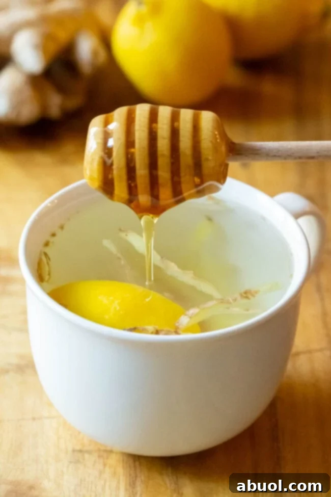 Honey being added to lemon ginger tea. A spoonful of raw honey being drizzled into a mug of freshly brewed lemon ginger tea.