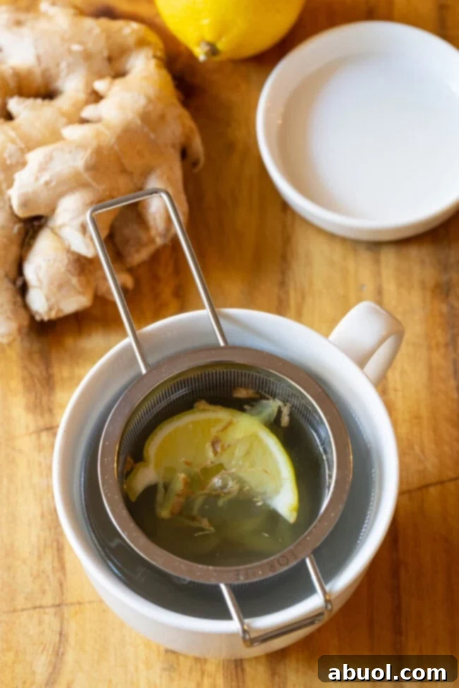 Lemon ginger detox tea in a mug with a tea infuser. A beautifully prepared mug of lemon ginger detox tea, with a stainless steel tea infuser submerged, capturing the essence of a healthy, comforting drink.