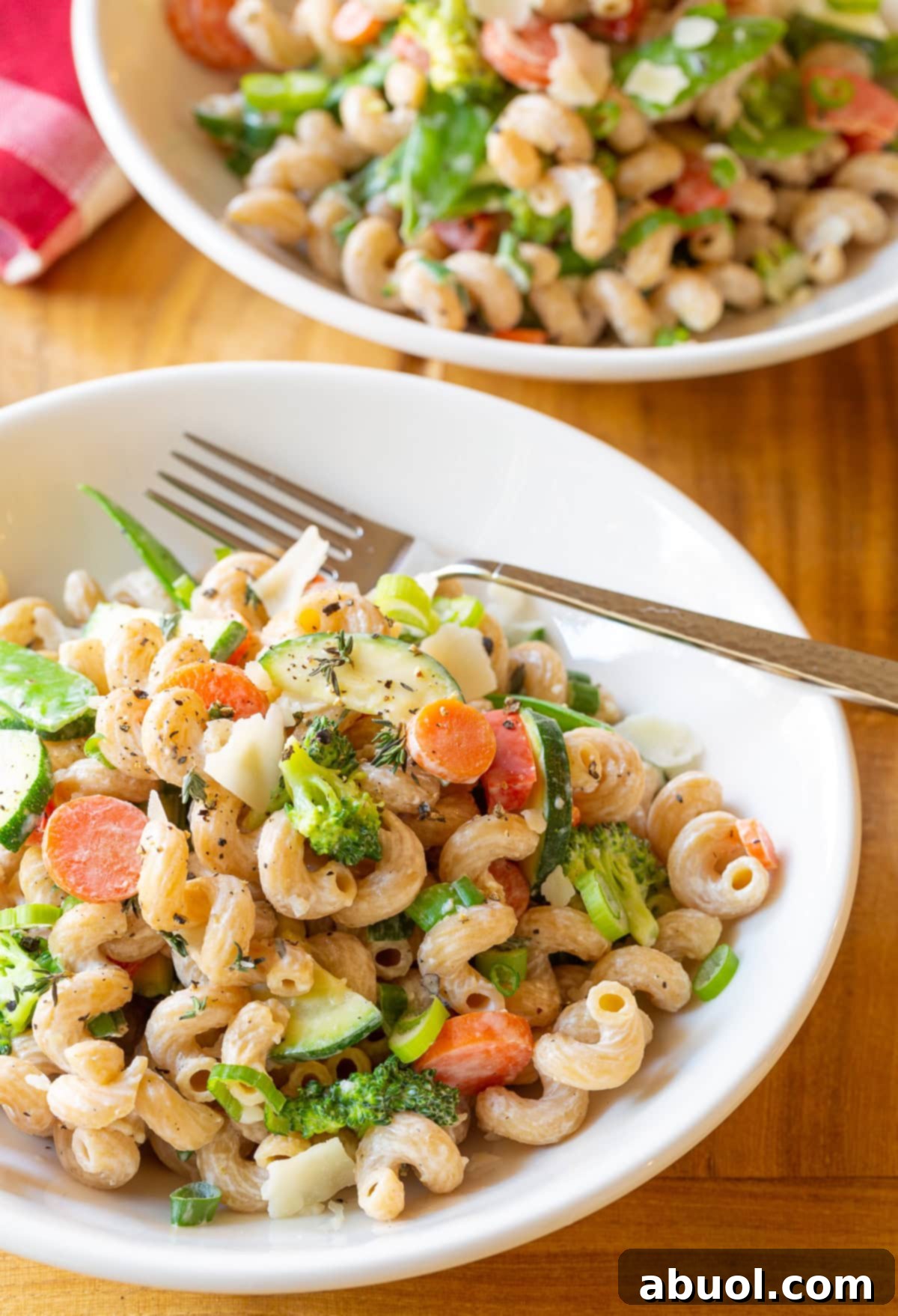 A large white bowl of skinny noodle primavera featuring vibrant chopped zucchini, carrots, broccoli, and red peppers, topped with shaved parmesan cheese, ready to be served.